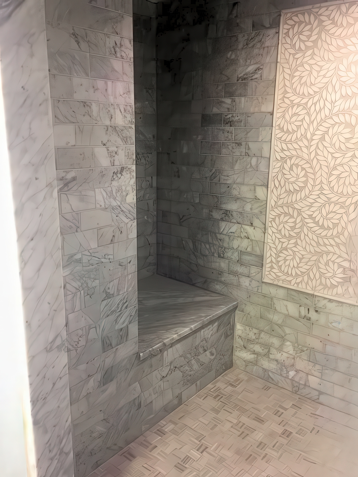 Marble walk-in shower with built-in bench seat and decorative leaf mosaic accent panels