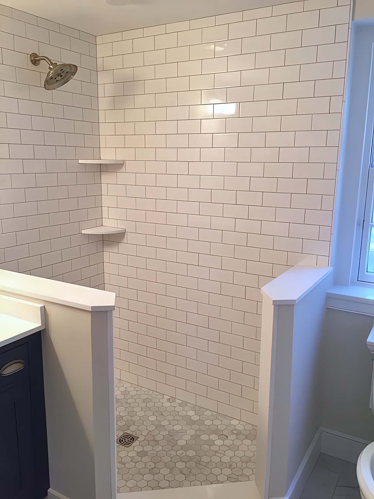 Walk-in shower with white subway tile walls, corner shelves, and hexagonal marble floor tile