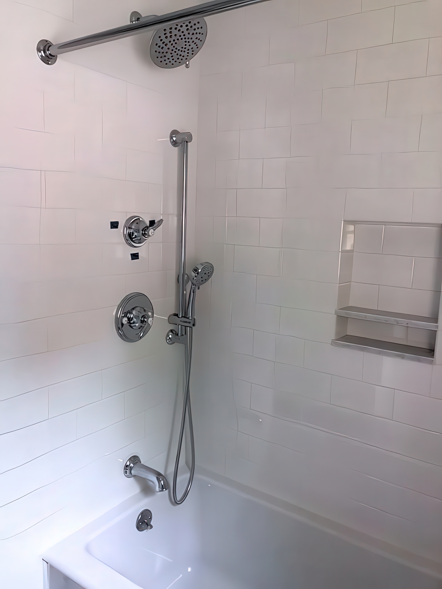 Tub/shower combo with white subway tile, rain and hand showerheads, and built-in niche