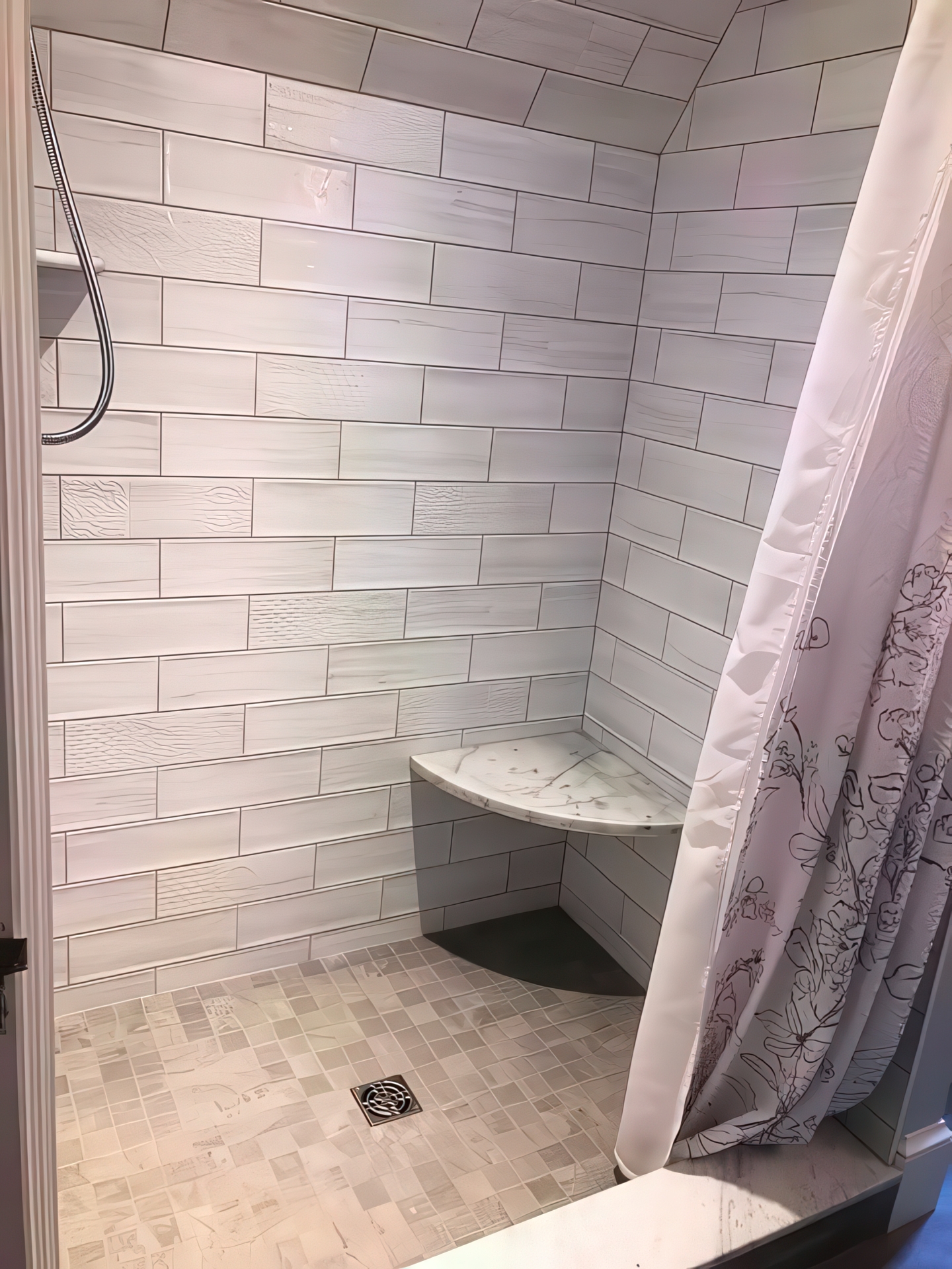 Walk-in shower wider view showing corner seat, mosaic floor tile, and curtain
