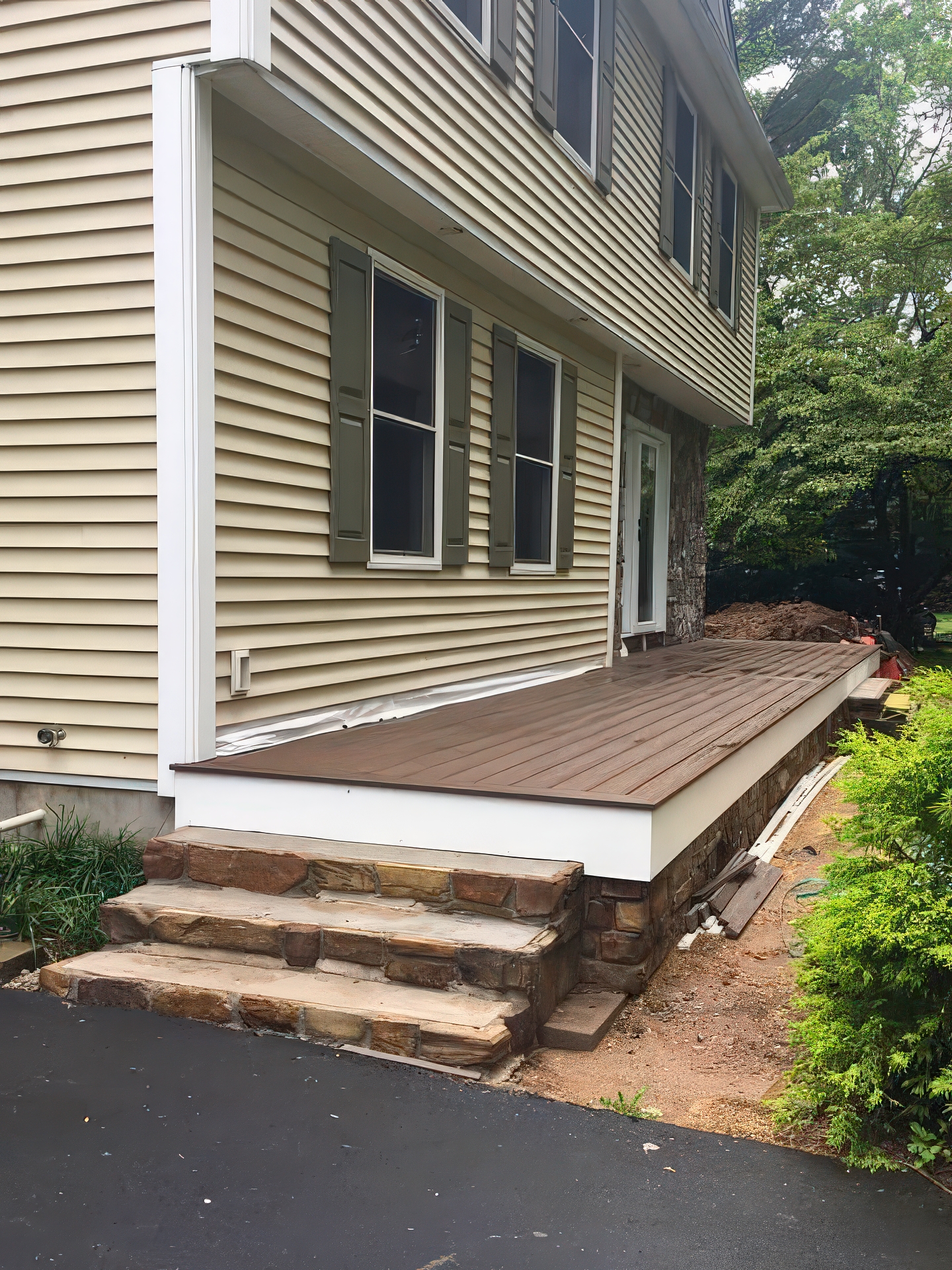 Side view of finished deck with composite boards, stone steps, and white fascia
