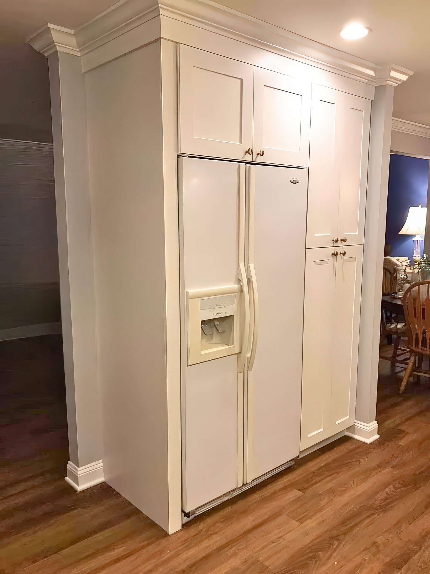 Built-in refrigerator surround with white cabinetry and crown molding