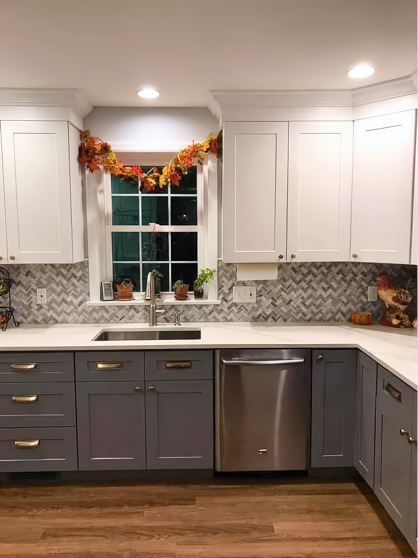 Kitchen sink under window with gray lower cabinets, herringbone backsplash, and dishwasher
