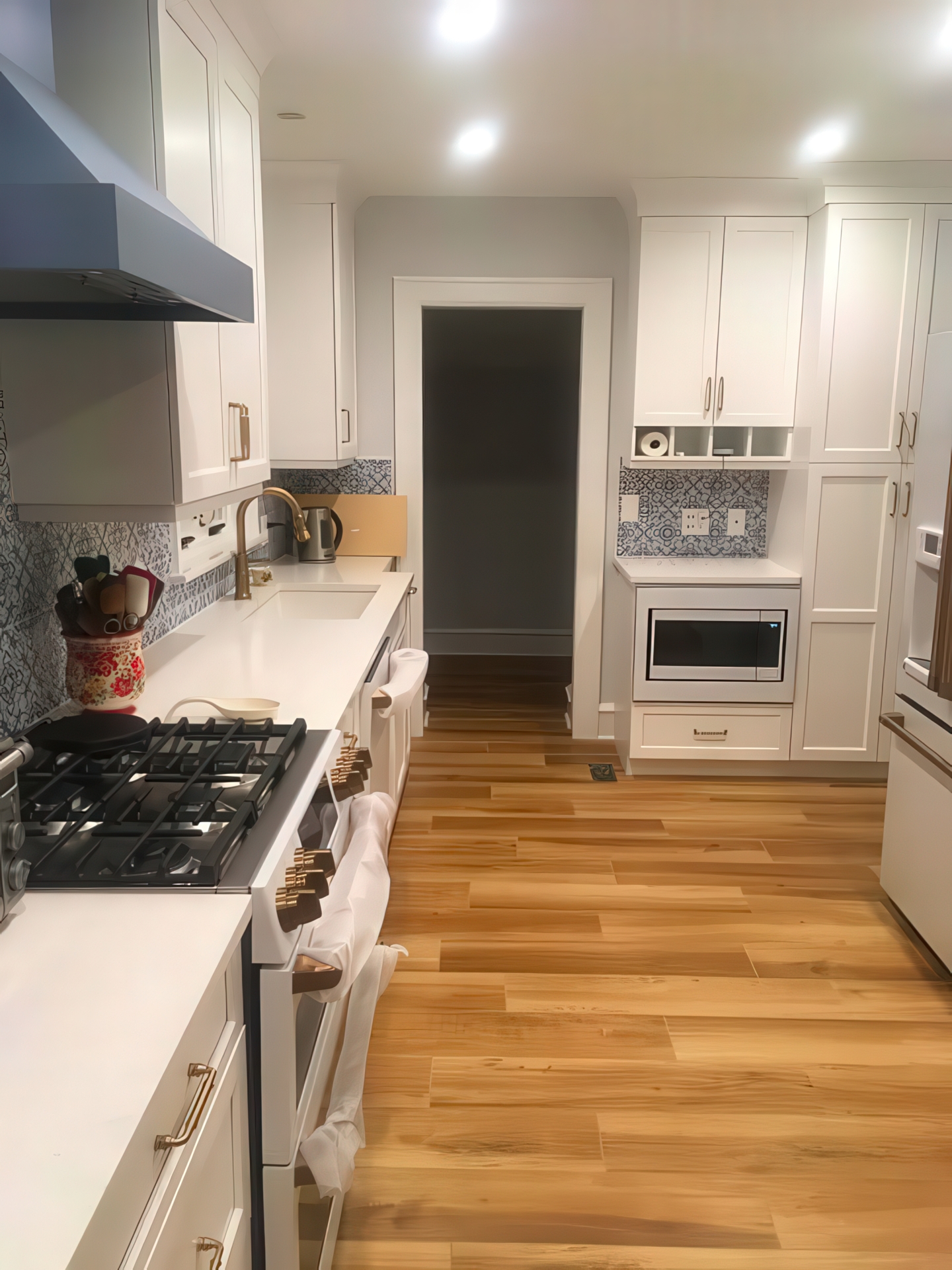 Remodeled galley kitchen with gas range, white cabinetry, and blue tile backsplash